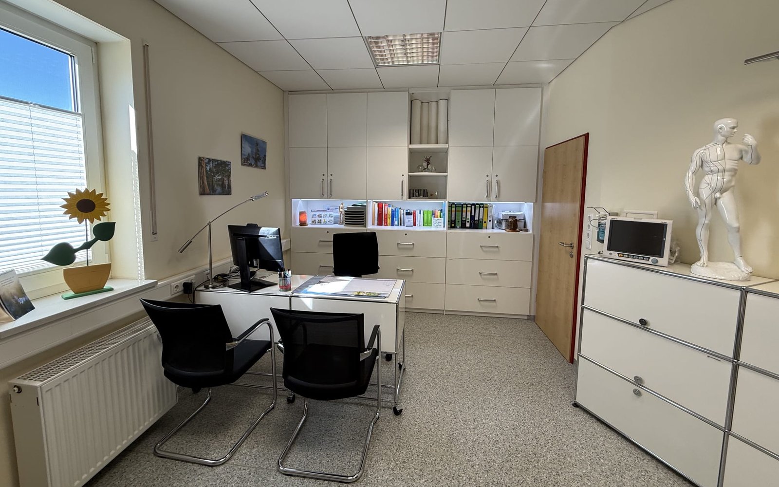 Sprech- und Behandlungszimmer der Praxis in Hof, mit Schreibtisch, Besucherstühlen und Überwachungsmonitor